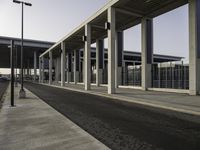 a building with metal columns and many cars parked at the roadside side and an open walkway