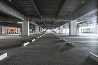 a long concrete sidewalk next to parking spaces in a building with concrete pillars and columns