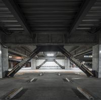 a long concrete sidewalk next to parking spaces in a building with concrete pillars and columns