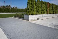 a sidewalk that has grass and trees along it along the walkway, along with a large concrete planter bed