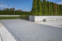 a sidewalk that has grass and trees along it along the walkway, along with a large concrete planter bed