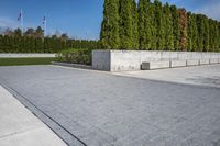 a sidewalk that has grass and trees along it along the walkway, along with a large concrete planter bed