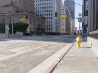 an empty city street in the daytime with a building on both sides of it and a yellow fire hydrant on the other side
