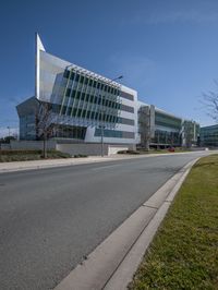 a big modern building is by the side of the street in front of some green grass