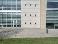 large white building with several windows on top of it, next to a sidewalk with grass, and an empty parking meter