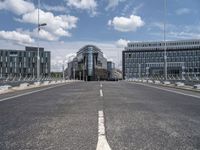 a paved, empty street in front of some modern buildings with tall windows and a sky background