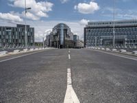 a paved, empty street in front of some modern buildings with tall windows and a sky background