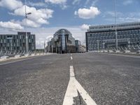 a paved, empty street in front of some modern buildings with tall windows and a sky background