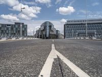 a paved, empty street in front of some modern buildings with tall windows and a sky background