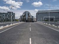 a paved, empty street in front of some modern buildings with tall windows and a sky background