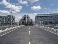 a paved, empty street in front of some modern buildings with tall windows and a sky background