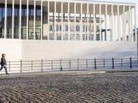 a woman walking in a long walkway near the waterfront on a sunny day near a large white building