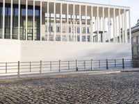 a woman walking in a long walkway near the waterfront on a sunny day near a large white building