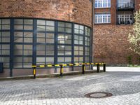 two black and yellow barriers at the back of a building in a brick area with several windows