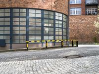 two black and yellow barriers at the back of a building in a brick area with several windows