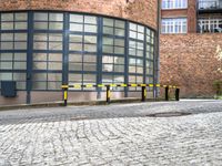 two black and yellow barriers at the back of a building in a brick area with several windows