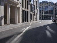 an empty street with some buildings and a car parked in front of it and sun on the road