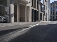 an empty street with some buildings and a car parked in front of it and sun on the road