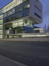 a modern building sits empty near a street at night with the lights on and no people in