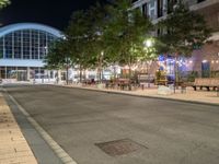 a street with many tables and chairs on both sides of the road at night by the city center