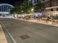 a street with many tables and chairs on both sides of the road at night by the city center