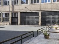 the side of an industrial building with a bench and stairs outside of it and a man that is walking