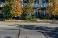 a fire hydrant on the side of a road near a building and sidewalk with trees