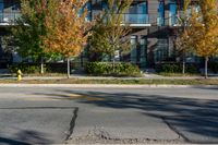 a fire hydrant on the side of a road near a building and sidewalk with trees