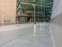 a large modern building with two white poles on the sidewalk in front of it and a person sitting on the ground