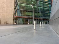 a large modern building with two white poles on the sidewalk in front of it and a person sitting on the ground