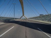 a truck driving across a bridge near a street corner near buildings and a bridge with many cables