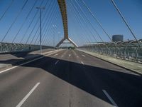 a truck driving across a bridge near a street corner near buildings and a bridge with many cables