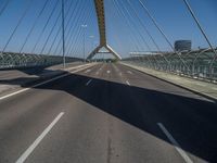 a truck driving across a bridge near a street corner near buildings and a bridge with many cables