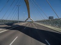 a truck driving across a bridge near a street corner near buildings and a bridge with many cables