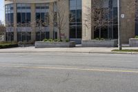 an empty street and building on the other side of it with some green bushes and bushes