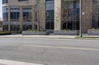 an empty street and building on the other side of it with some green bushes and bushes