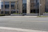 an empty street and building on the other side of it with some green bushes and bushes