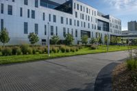 a walkway with shrubs on both sides of the street next to the large building behind