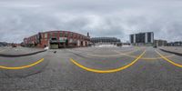 a cloudy sky and an empty parking lot with buildings in the backrouground and street signs painted yellow