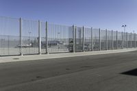 an asphalt road with a fence separating the sidewalk to a large airport area with luggage