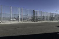 an asphalt road with a fence separating the sidewalk to a large airport area with luggage