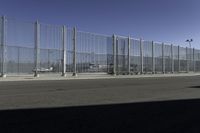 an asphalt road with a fence separating the sidewalk to a large airport area with luggage