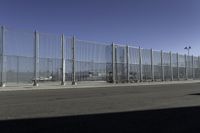 an asphalt road with a fence separating the sidewalk to a large airport area with luggage