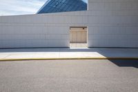 a closed door in the white building on a street corner with pavement and yellow curb