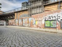 a brick building with graffiti and windows near the sidewalk and stairs and a bridge over it