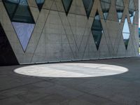 a shadow is seen on the pavement in front of a building with windows and triangles