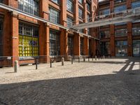 the buildings are in one block of bricked walkway with an overhead walkway on one side, surrounded by a metal fence