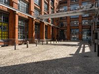 the buildings are in one block of bricked walkway with an overhead walkway on one side, surrounded by a metal fence