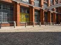 the buildings are in one block of bricked walkway with an overhead walkway on one side, surrounded by a metal fence