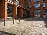 the buildings are in one block of bricked walkway with an overhead walkway on one side, surrounded by a metal fence